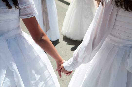 Dos niñas vestidas de primera comunión se dan la mano en la calle.