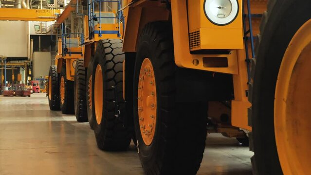 An assembly line of large dump trucks. Assembled trucks are lined up in the production hall. Production of large yellow BelAZ mining trucks. Close-up view