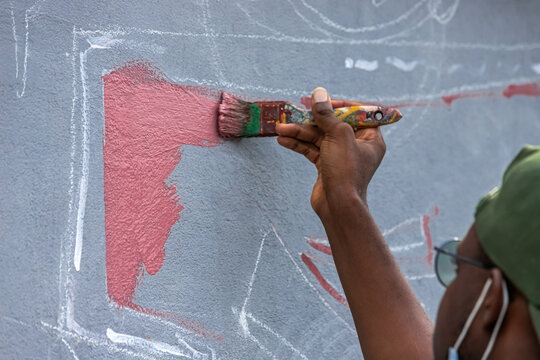 A Dedicated Young Artist Engaging With The Community As They Paint A Collaborative Mural, Fostering A Sense Of Unity And Pride In The Neighborhood.