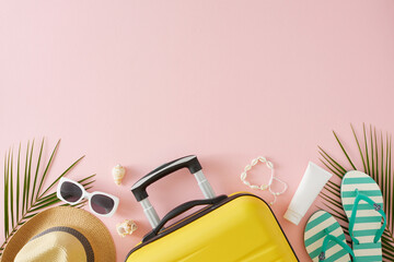 Summer travel theme. Top view flat lay of suitcase, beach accessories, seashells and sunscreen bottle with palm leaves on pastel pink background with empty space for text