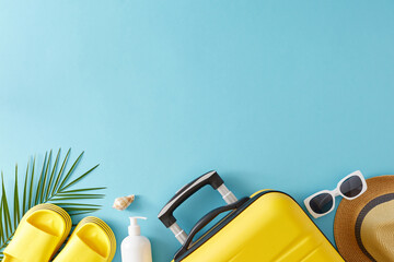 Concept of summer vacation. Top view flat lay of suitcase, sun-hat, flip-flops, sunglasses and sunscreen bottle with palm leaves on pastel blue background with blank space
