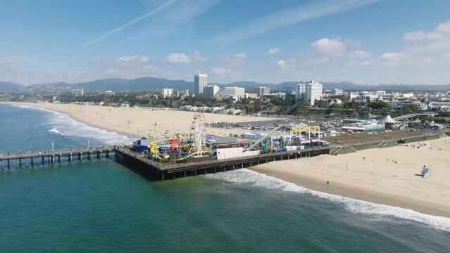 Santa Monica Pier on sunny summer day Los Angeles. Aerial footage of amusement park on historic Santa Monica pier from ocean side. Beautiful panorama of city skyline on background of sandy beach 4K