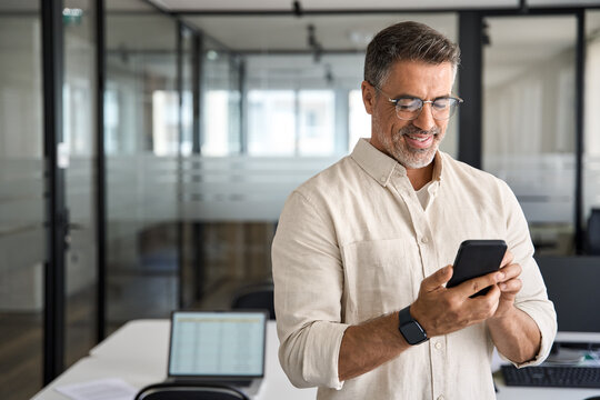 Copy space are with smiling mature Latin or Indian businessman holding smartphone in office. Middle aged manager using cell phone mobile app. Digital technology application and solutions for business.
