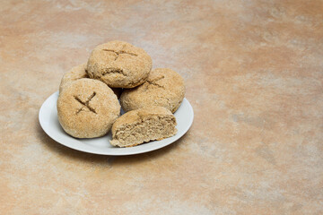 A small white plate placed on a rustic stone-like kitchen countertop with freshly baked homemade whole wheat bread rolls, with one of them sliced in half to reveal its crumb texture and copy space.
