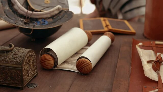 Vintage details on wooden table in military camp, old paper manuscript in leather cover, vintage metal jewelry box, protective helmet called galea in legion's tent. Daily life of Roman legionaries of