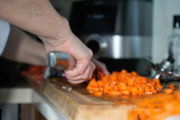 Hands only. Women are slicing carrots with a knife on a wooden board. High quality photo