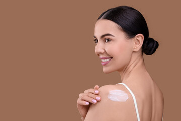 Beautiful woman with smear of body cream on her shoulder against light brown background, space for...