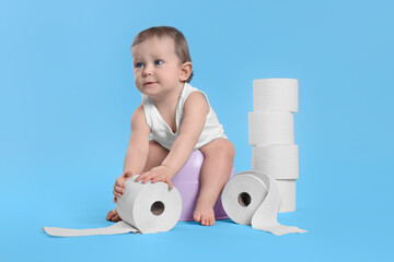 Little child sitting on baby potty and stack of toilet paper rolls against light blue background