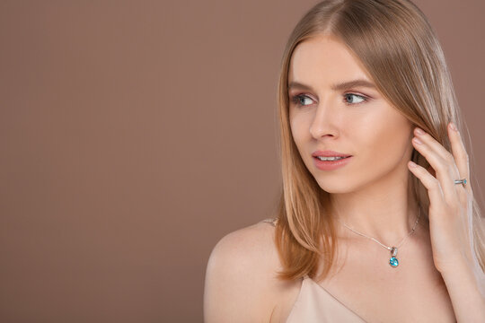 Beautiful young woman with elegant jewelry on light brown background, space for text