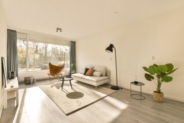 a living room with white walls and wood flooring in the center of the room, there is a large window looking out to