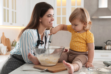 Mother and her little daughter cooking dough together in kitchen