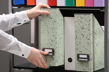 Woman taking folder from shelf in office, closeup