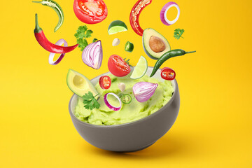 Delicious guacamole with flying ingredients on yellow background