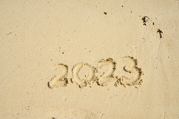 The year 2023 is painted on the sand on a sandy beach.