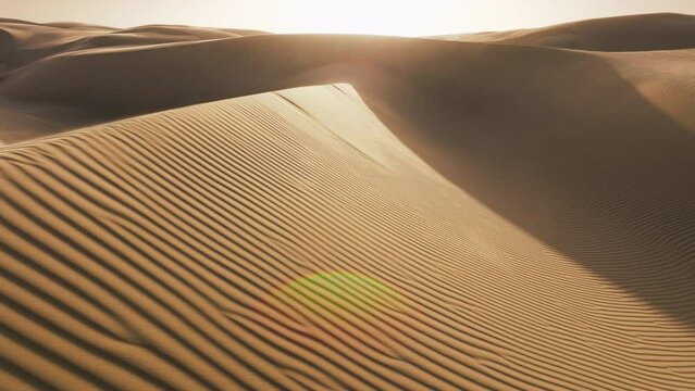 Incredible shot strong wind blowing away shiny golden sand from top of rippled dunes in sunset light. Cinematic aerial background with ripples texture on sand surface in desert nature in low sunshine