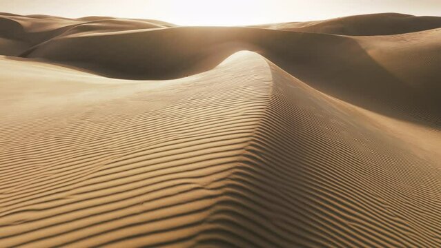 Close up of rippled texture on sand surface in desert nature in low sunshine. Incredible shot strong wind blowing sand. Shiny golden sand on top of rippled dunes in sunset cinematic aerial background