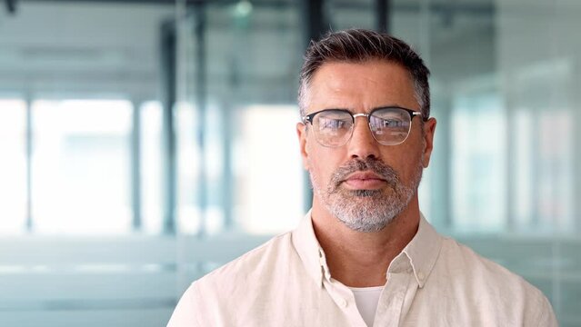 Headshot close up portrait of indian or latin confident mature good looking middle age leader, ceo male businessman on blur office background. Handsome hispanic senior business man smiling at camera.