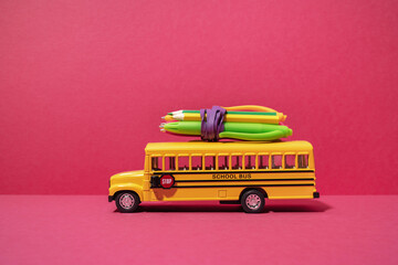 School bus with with pencils and pens on top onmagenta red background. Back to school. Delivery...