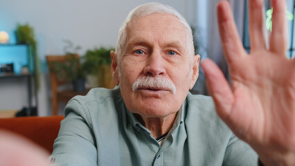 POV of senior grandfather man making online selfie video call talking waving hand looking at camera at home apartment indoors. Communication, meeting. Elderly blogger making smartphone conversation - Powered by Adobe
