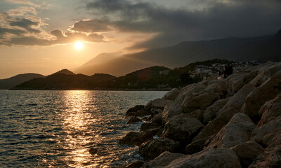 A magnificent beach scenery with a majestic mountain and rocky shore, bathed in the warm sunlight of an orange sunset. A perfect moment to admire natures beauty on Turkeys Kas coast.