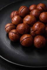 Delicious roasted macadamia nuts in shell on a dark textured background