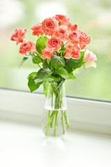 Fototapeta na wymiar Beautiful tender pink roses in glass vase on windowsill in room. Bouquet of the flowers in home interior. Selective focus.