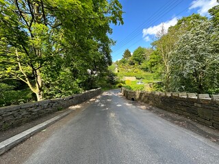 View down a country road, with old trees, a stone bridge, and a distant hillside on, Shutts lane, Norwood Green, UK