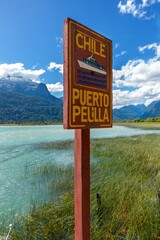 Vertical Information Post Table at Puerto Peulla Boat Dock Lake Crossing, Todos Los Santos Lake, Chile with Distant Andes Mountain Peaks Landscape in the Background