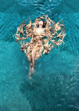 Top view of a beautiful sexy woman with vitiligo disease and dark hair relaxed in dried up leaves, of a banana tree in heart shape happily floating in turquoise water in the pool, copy space