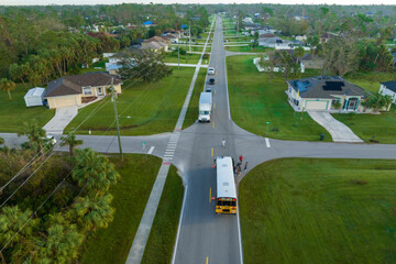 Aerial view of american yellow school bus picking up children at sidewalk bus stop for their...