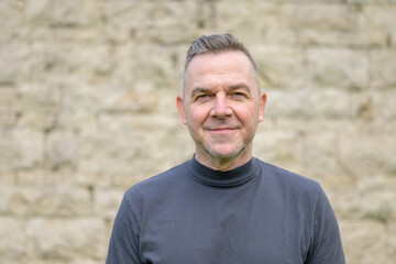 Grey haired man standing in front of a wall