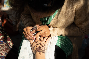 A student of the master applies a henna pattern to a woman's hand in a trial lesson