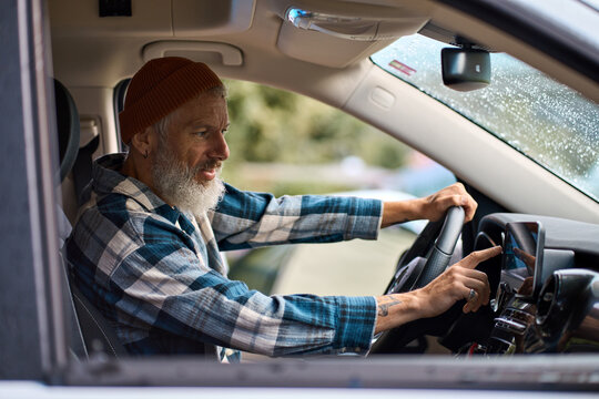 Older man sitting in camper van using gps navigation map system digital device. Smiling mature active traveler driving car vehicle looking at screen touching sensor gadget dashboard on the way.