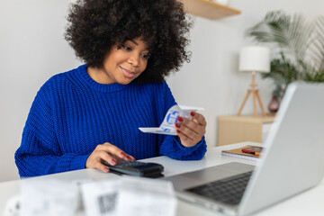 Young latin woman with laptop computer managing budget and expenses bills at home. African american...