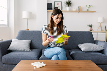 Young pretty woman reading menstrual cup use instructions sitting on sofa at home