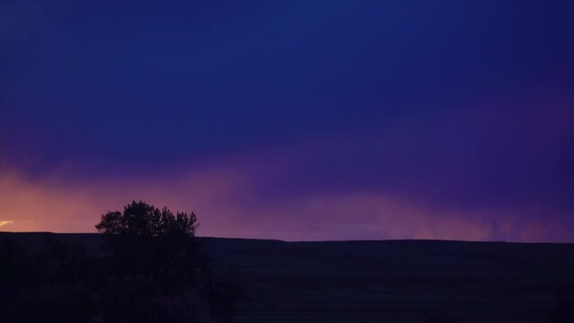 Purple clouds drop rain over pink sunset prairie