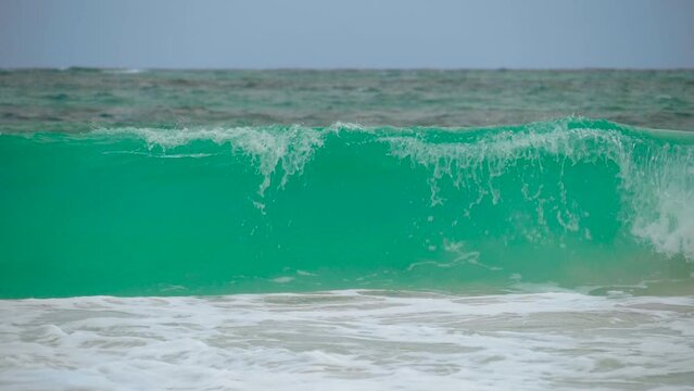 Ocean shorebreak in front view. Big beautiful green blue wave splashing with backwave and ready to break out. White foam sliding over sand. Beautiful sea waves. Beach sand and amazing sea.