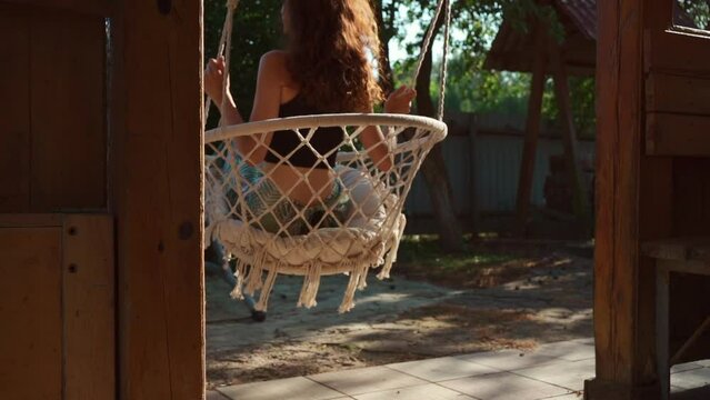 young female riding on macrame swing chair at country house terrace outdoors