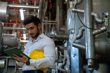 Professional electrical engineer in safety uniform working on digital tablet at factory site. Industrial technician worker maintenance and checking power control system at manufacturing plant room.