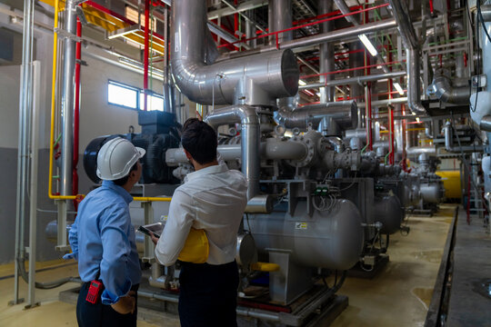 Two professional electrical engineer in safety uniform working together at factory site control room. Industrial engineer worker checking maintenance electric system on laptop computer at plant room.