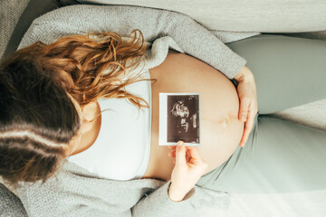 Top view of a woman sitting on a sofa looking at an ultrasound image of her baby in the last stage...