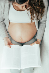 Top view of a woman sitting on a sofa reading a book in the last stage of pregnancy. Pregnancy...