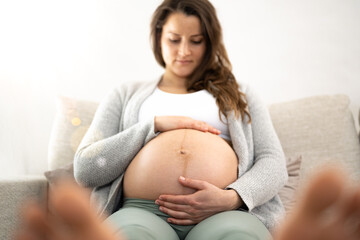 Frontal view of woman sitting on a sofa gently holding her belly in expectation of the baby during the last stage of pregnancy. Pregnancy third trimester - week 34. Front view. White background.