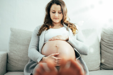 Frontal view of happy woman sitting on sofa gently holding her belly in imagination of baby in last stage of pregnancy. Pregnancy third trimester - week 34. Front view. White background.
