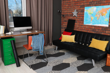Stylish teenager's room with computer, black sofa and world map on brick wall