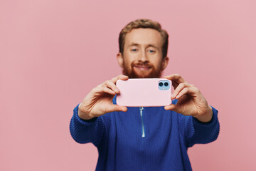Portrait of a redheaded man with phone in hand taking selfies and photos on his phone with a smile...