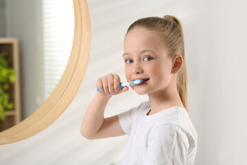 Cute little girl brushing her teeth with plastic toothbrush in bathroom, space for text