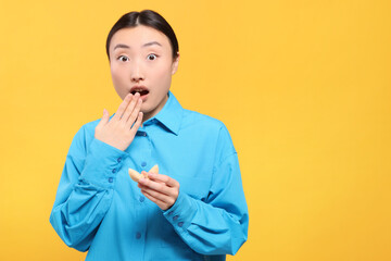 Surprised asian woman holding tasty fortune cookie with prediction on yellow background, space for text