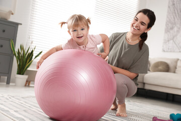 Fototapeta premium Mother doing exercise with her daughter on fitball at home