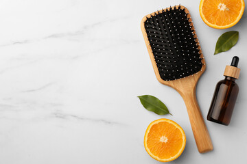 Wooden hair brush, bottle of essential oil and orange slices on white marble table, flat lay. Space...